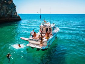 A lively group enjoys a day on the water, with some swimming and others on a paddleboard, showcasing the perfect blend of fun and adventure aboard their boat.