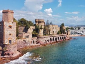 A scenic view of a historic castle by the water, showcasing beautiful architecture and a marina in the background.