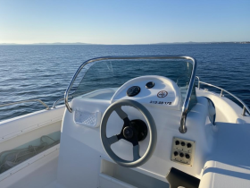 A close-up view of the helm and console of a boat, showcasing the steering wheel and control panel against a serene water backdrop.