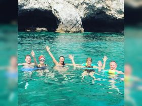 A cheerful group of friends enjoys a refreshing swim in crystal-clear turquoise waters near a stunning cave — perfect for memorable summer adventures.