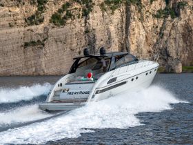 A sleek speedboat named 'MERYROSE' glides through the water, showcasing its elegant design against a stunning rocky backdrop.