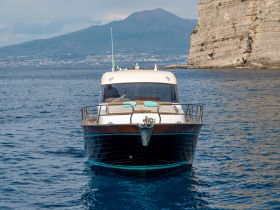 A stunning yacht glides through the clear waters, showcasing its elegant design against the backdrop of a mountainous coastline.