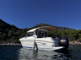 A sleek view of a motorboat anchored in calm waters, showcasing its elegant design against a backdrop of lush greenery and rocky shoreline.