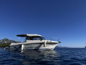A sleek speedboat anchored in clear waters, showcasing its elegant design against a stunning backdrop of mountains and a clear blue sky.