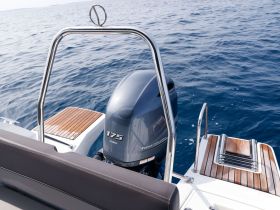 A close-up view of the outboard motor on a sleek boat, showcasing the vessel's design and craftsmanship against a serene blue ocean backdrop.