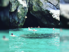 A group of friends enjoys swimming in crystal-clear waters near a rocky cave, creating a perfect backdrop for a fun day on the water.
