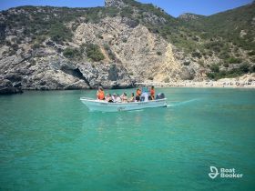 A lively group enjoys a boat tour in crystal-clear waters, surrounded by stunning rocky landscapes and a beach in the background — perfect for summer adventures.