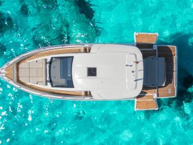 A stunning aerial view of a sleek boat gliding over crystal-clear turquoise waters, showcasing its elegant design and spacious deck.