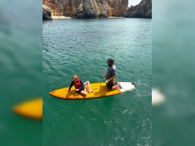 A child and an adult enjoy paddleboarding in clear waters, surrounded by stunning cliffs — a perfect day for water activities and family fun.