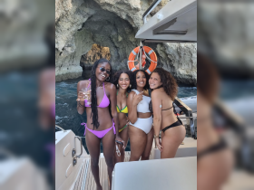 A joyful group of friends poses on a boat, enjoying drinks and celebrating their time together in a stunning coastal setting.