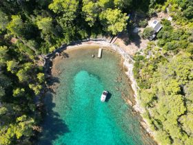 A stunning aerial view of a secluded cove with crystal-clear turquoise waters and a boat anchored nearby, perfect for exploring hidden gems along the coastline.