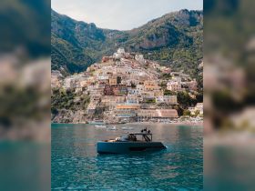 A sleek boat is anchored in clear waters, showcasing the stunning coastal town of Positano in the background, perfect for scenic boat tours along the Amalfi Coast.
