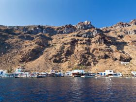 A picturesque view of a harbor nestled against rugged cliffs, showcasing vibrant buildings and lively activity — a perfect destination for island exploration.