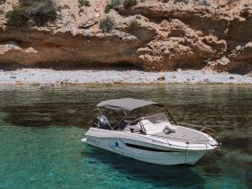 A sleek speedboat is docked in crystal-clear waters, surrounded by rocky cliffs, perfect for a day of exploration and relaxation.