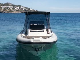 A sleek boat is anchored in clear turquoise waters, showcasing its modern design against a picturesque coastal backdrop.