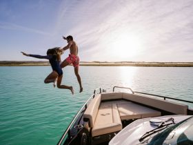 A couple joyfully leaps off the boat into the turquoise waters, capturing the essence of summer fun and adventure on the water.