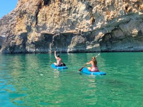A couple enjoys paddleboarding in clear turquoise waters, surrounded by stunning rock formations — a perfect adventure for nature lovers.