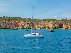 A catamaran sails through crystal-clear waters, showcasing stunning coastal cliffs — a perfect scene for a memorable boating adventure.