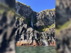 A stunning view of cascading waterfalls against a rugged coastline, showcasing the natural beauty of the area — perfect for nature lovers and adventure seekers.