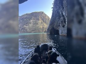 A group of adventurers explores a stunning cave entrance by boat, surrounded by towering cliffs and crystal-clear waters — a perfect setting for unforgettable excursions.