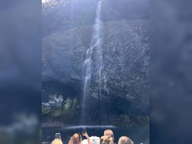 Guests capture the stunning waterfall cascading down rocky cliffs while enjoying a boat tour — a breathtaking highlight of their adventure.