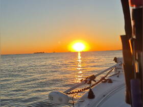 A stunning sunset view from the bow of a boat, with the sun reflecting on the water — perfect for serene evening cruises.