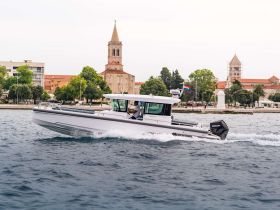 A sleek speedboat navigates the waters, showcasing its design against a picturesque coastal backdrop, ideal for thrilling adventures on the sea.