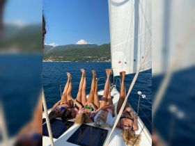A group of friends enjoys a sunny day sailing, playfully posing with their legs in the air on the deck — a perfect moment of summer fun on the water.