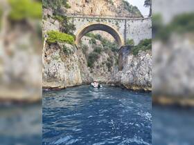 A scenic view of a boat navigating through a narrow coastal passage beneath a historic bridge, showcasing the stunning natural beauty of the area.