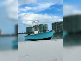 A vibrant speedboat rests on the sandy shore, framed by modern buildings and a clear blue sky, perfect for a day of fun on the water.