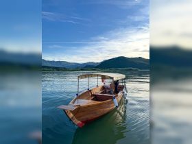 A charming wooden boat glides through calm waters, surrounded by scenic mountains — perfect for leisurely explorations or fishing trips.