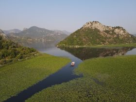 A stunning aerial view of a serene lake surrounded by lush greenery and mountains, with a small boat navigating through the water — a perfect escape into nature.