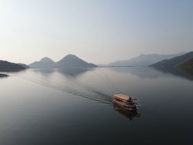 An aerial view of a boat gliding across a serene lake, surrounded by majestic mountains — a perfect scene for nature lovers and adventure seekers.