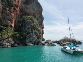 A picturesque view of a sailboat anchored near stunning rock formations and turquoise waters, showcasing the beauty of island exploration.