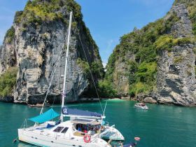 A stunning view of a catamaran anchored in turquoise waters surrounded by dramatic cliffs, showcasing the beauty of island adventures.