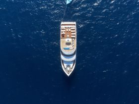 A stunning aerial view of a luxurious yacht cruising through deep blue waters, showcasing its elegant design and spacious deck — perfect for upscale charters and ocean adventures.