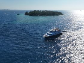 A stunning aerial view of a yacht cruising through vibrant blue waters, with a picturesque island in the background, perfect for showcasing luxury boating experiences.