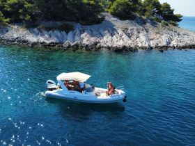 A couple enjoys a sunny day on a boat near a rocky coastline, perfect for summer adventures and island exploration.