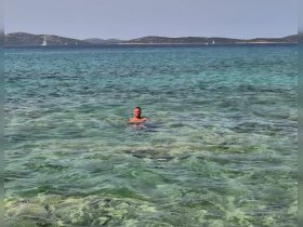 A man enjoys a refreshing swim in crystal-clear waters, surrounded by scenic islands — a perfect highlight of a summer boating adventure.
