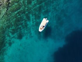 A stunning aerial view of a boat gliding over crystal-clear waters, showcasing the vibrant underwater scenery — perfect for exploring coastal destinations.