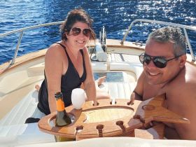 A couple enjoys drinks and sunshine on the deck of a boat, perfect for a relaxing day on the water.