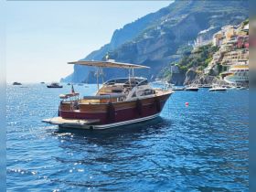 A stunning yacht anchored in crystal-clear waters, with picturesque cliffs and colorful buildings in the background, perfect for exploring coastal destinations.
