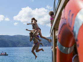 A group of kids joyfully jumps off a boat into the sparkling blue waters, capturing the essence of summer fun and adventure on the water.