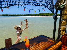 A joyful scene at the beach with a woman and two children playing in the water, while a colorful cocktail sits on the bar — perfect for family fun and relaxation under the sun.