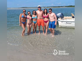 A lively group of friends enjoys a sunny day at the beach, wading in the water next to their boat — perfect for summer adventures and beach outings.