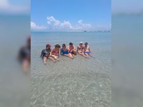 A group of friends enjoys a sunny day at the beach, relaxing in shallow water — perfect for summer fun and memorable outings.