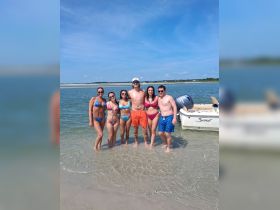 A lively group of friends enjoys a sunny day at the beach, splashing in the water near their boat — perfect for summer fun and memorable gatherings.