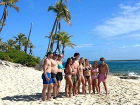 A cheerful group poses for a photo on a beautiful beach, surrounded by palm trees and clear blue waters — capturing the essence of a fun vacation.