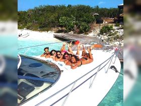A fun group of friends relaxes on the bow of a boat, enjoying the sun and turquoise waters — perfect for beach parties and summer adventures.