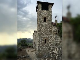 A stone tower and building set against a cloudy sky, showcasing rustic architecture and mountainous scenery.